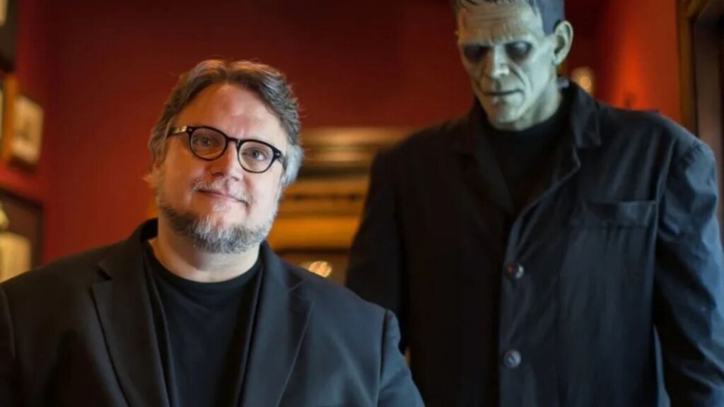 Diretor Guilhermo Del Toro posando ao lado de uma estátua do monstro de Frankeisten
