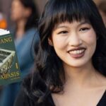 Autora Rebecca Kuang sorrindo para a foto com um vestido preto, junto ao seu novo livro: katabassis.